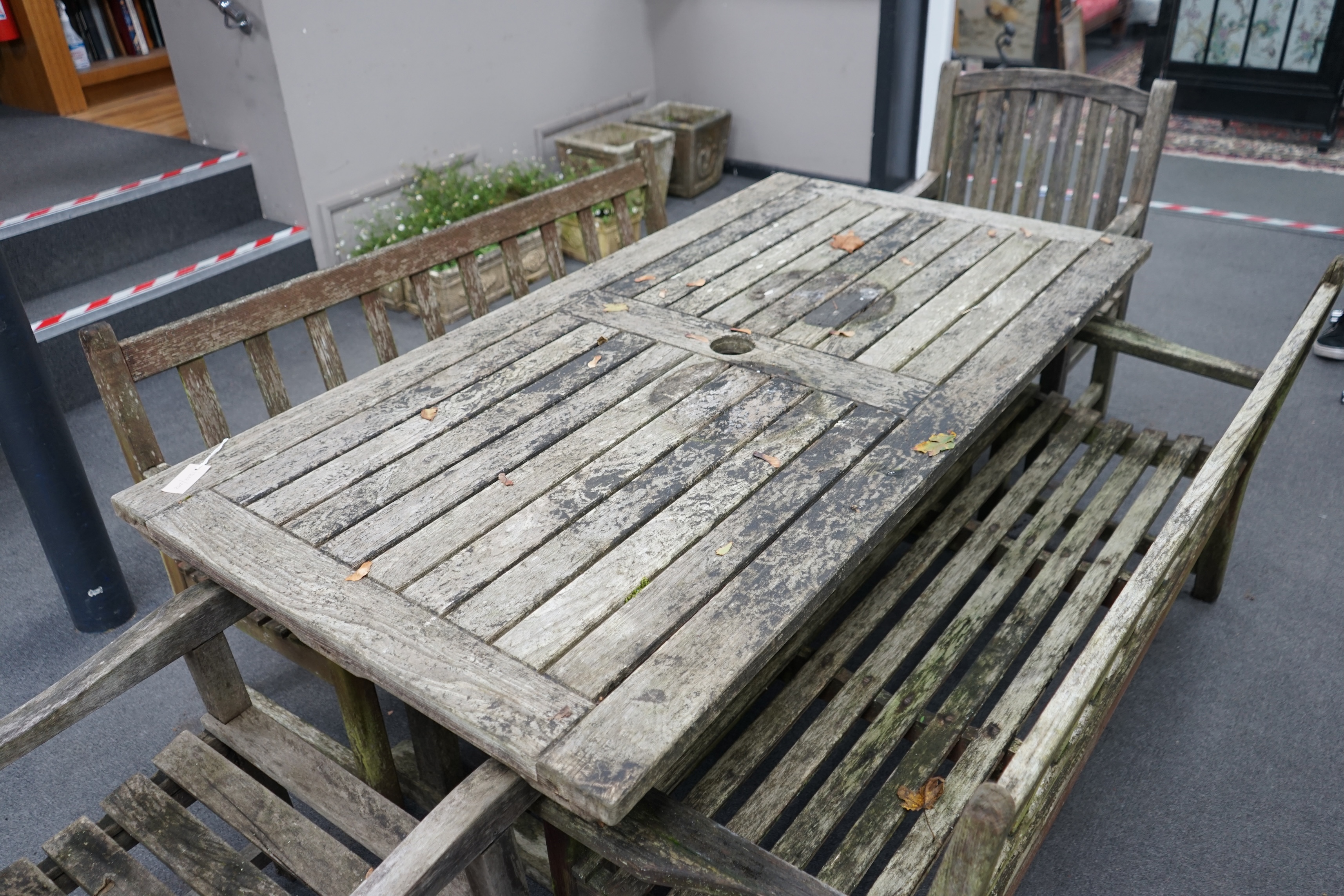 A weathered teak extending garden table, with pair of matching slatted benches and two elbow chairs